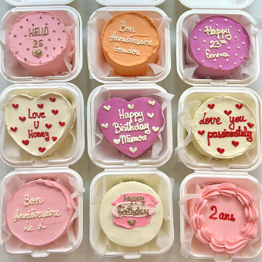Small round cakes in clear containers with personalized messages on a light background