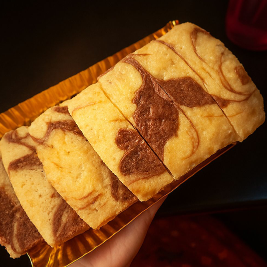 Marbled cookies on a gold tray held by a hand against a dark background