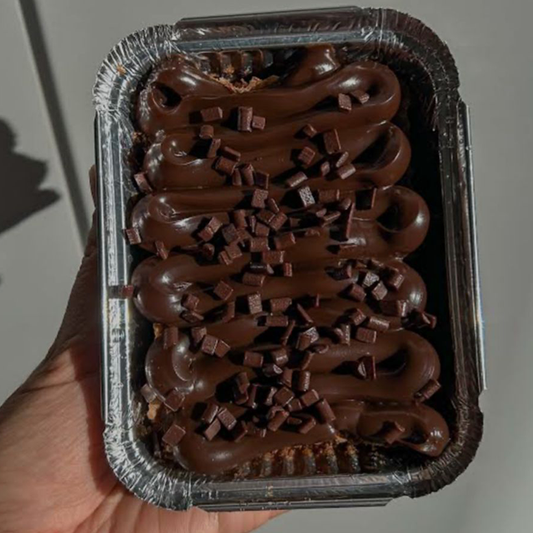 Chocolate dessert in a foil container held by a hand against a neutral background
