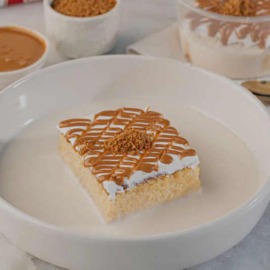 Square dessert with caramel drizzle on a white plate, surrounded by bowls of caramel and whipped cream.